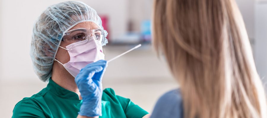 Well-protected medical staff performs swab test for Covid-19 to a young blonde female patient.